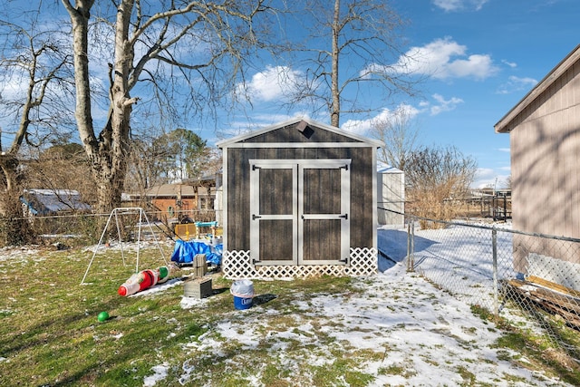 snow covered structure with an outbuilding, a playground, a fenced backyard, and a storage unit