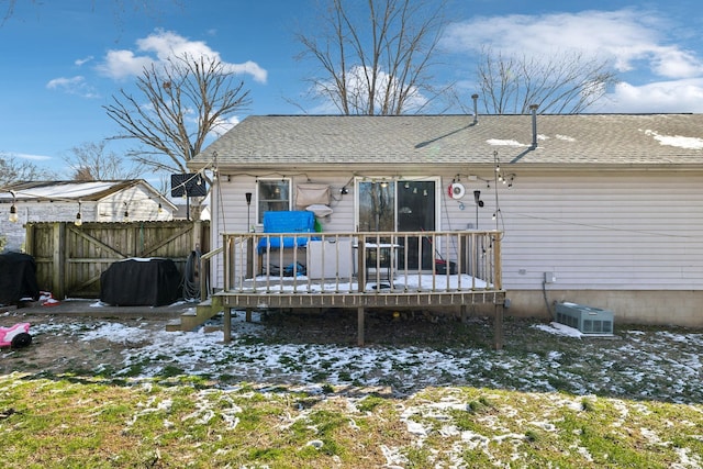 snow covered property featuring a shingled roof, fence, and a deck