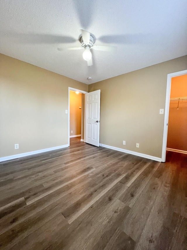 empty room with a ceiling fan, a textured ceiling, baseboards, and dark wood-style flooring