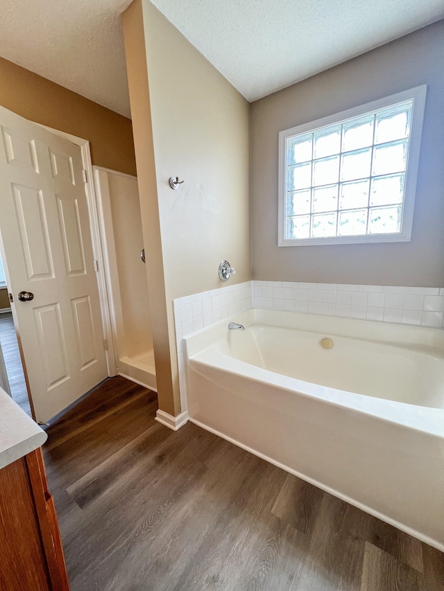 bathroom with a stall shower, wood finished floors, a textured ceiling, vanity, and a bath