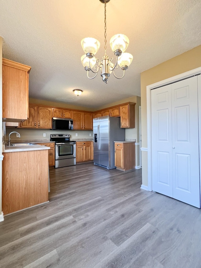 kitchen with appliances with stainless steel finishes, brown cabinets, light countertops, pendant lighting, and a notable chandelier