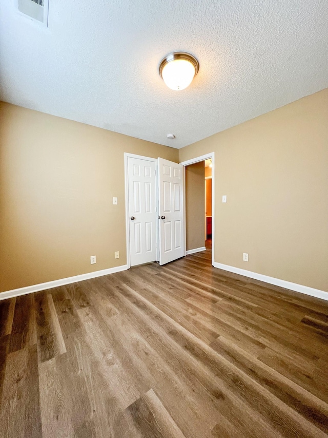 unfurnished bedroom featuring visible vents, a textured ceiling, baseboards, and wood finished floors