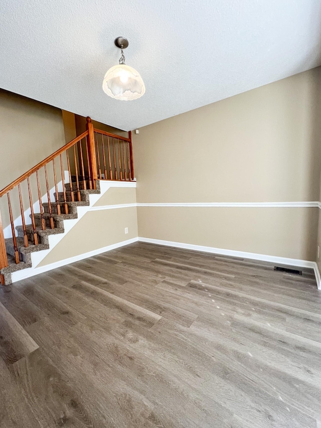 empty room featuring stairway, a textured ceiling, baseboards, and wood finished floors