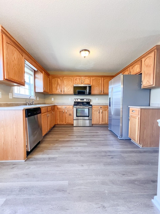 kitchen featuring light wood finished floors, light countertops, appliances with stainless steel finishes, a sink, and a textured ceiling