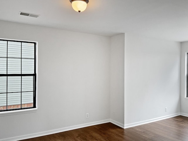 empty room with dark wood-style flooring, visible vents, and baseboards