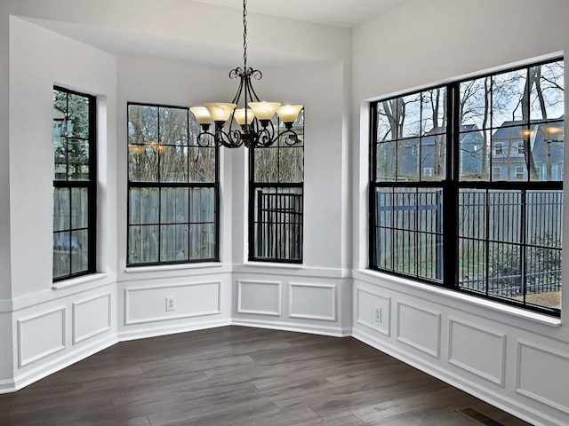 unfurnished dining area featuring an inviting chandelier, visible vents, a decorative wall, and dark wood-type flooring