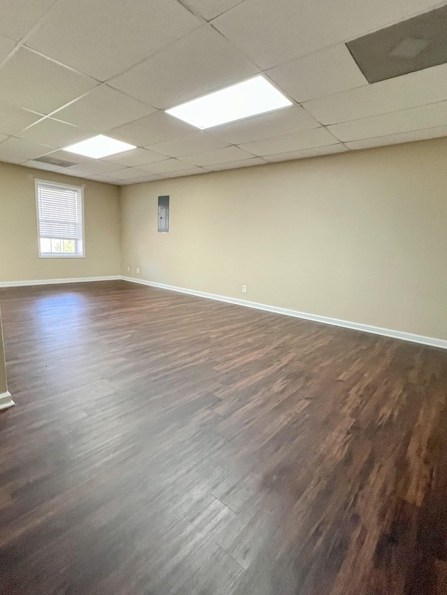 empty room with a drop ceiling, dark wood finished floors, and baseboards