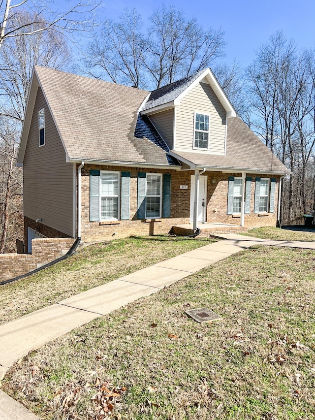 view of front facade with roof with shingles, a front lawn, and brick siding