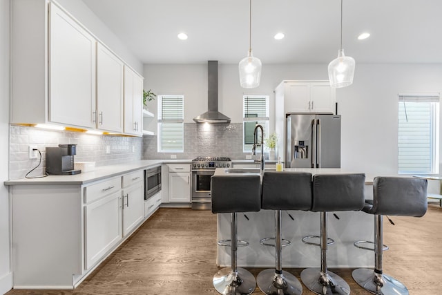 kitchen with white cabinets, wall chimney range hood, appliances with stainless steel finishes, and light countertops