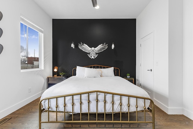 bedroom with dark wood-style floors, an accent wall, and baseboards