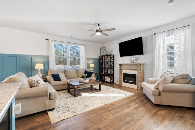 living room with a glass covered fireplace, plenty of natural light, wood finished floors, and a ceiling fan