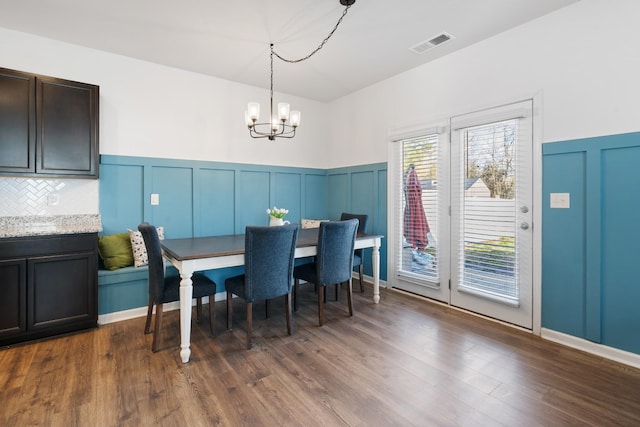 dining area with a decorative wall, a wainscoted wall, dark wood-style flooring, visible vents, and an inviting chandelier