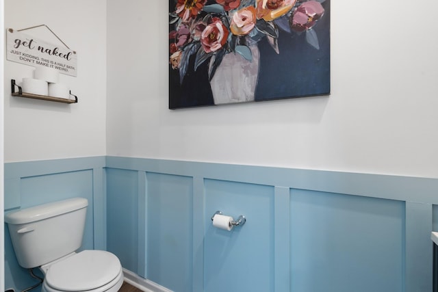 bathroom with toilet, a decorative wall, and wainscoting