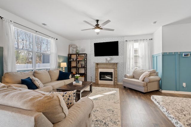 living room with ceiling fan, a wainscoted wall, a high end fireplace, visible vents, and dark wood-style floors