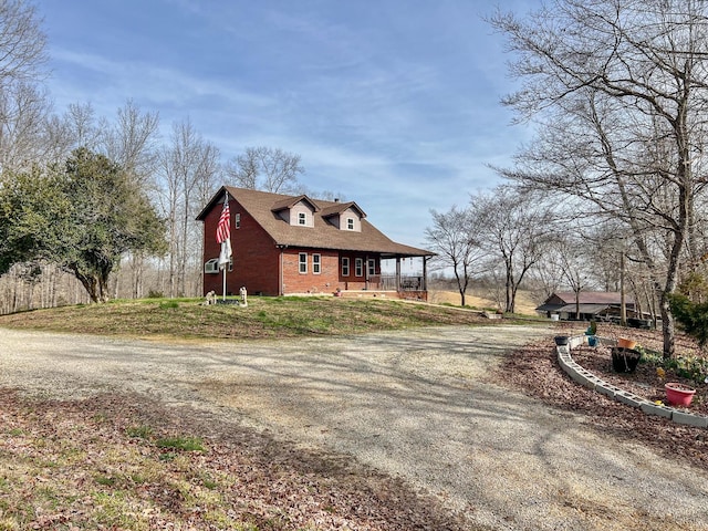 view of property exterior featuring covered porch, brick siding, and gravel driveway