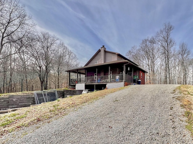 view of front facade featuring a porch, a chimney, and gravel driveway