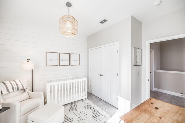 bedroom featuring light colored carpet, visible vents, baseboards, a closet, and a nursery area