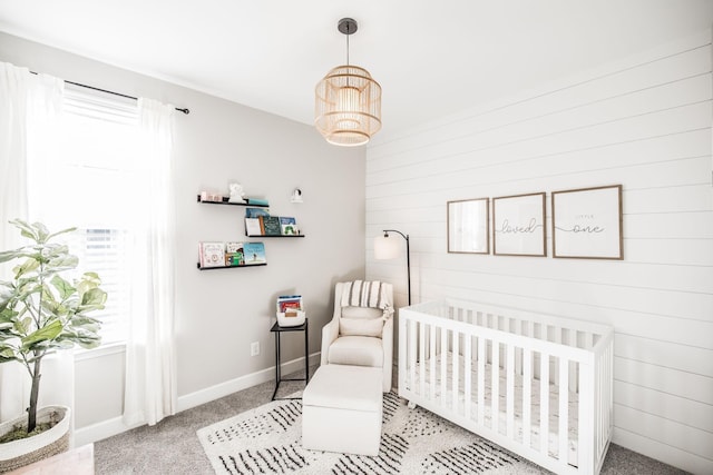 bedroom with a nursery area, light colored carpet, wooden walls, and baseboards