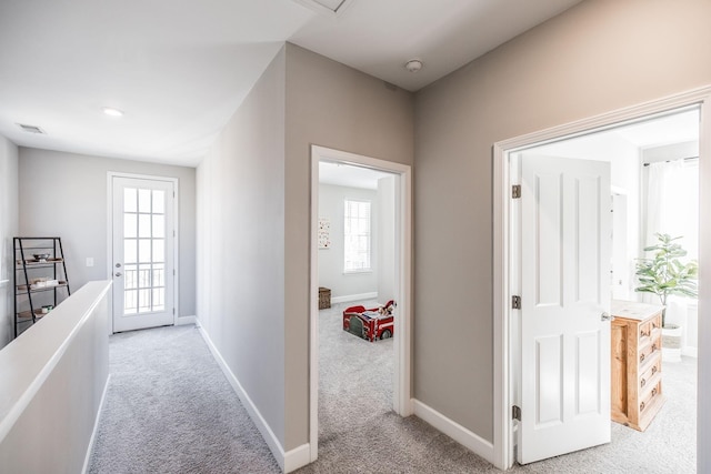 hall featuring light colored carpet, visible vents, and baseboards