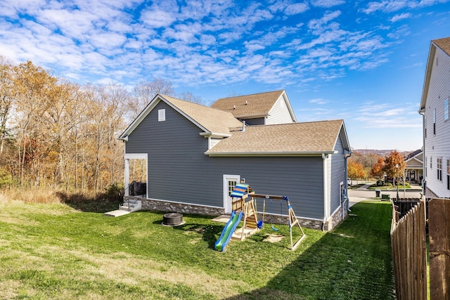 rear view of property with a shingled roof, a playground, a yard, and fence