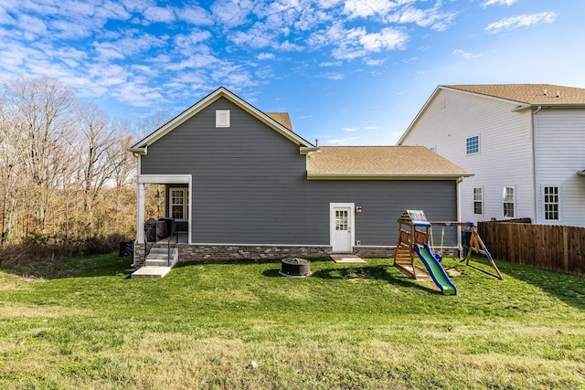 back of property with fence, a lawn, and a playground