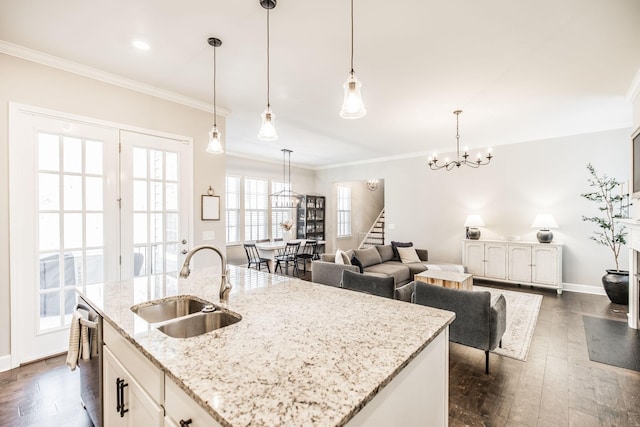 kitchen featuring pendant lighting, ornamental molding, white cabinets, a sink, and an island with sink