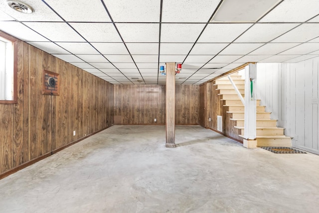 below grade area with a paneled ceiling, stairway, visible vents, and wooden walls