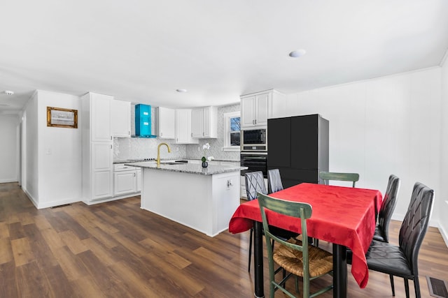 kitchen featuring dark wood-style flooring, a center island with sink, white cabinets, light stone countertops, and built in microwave