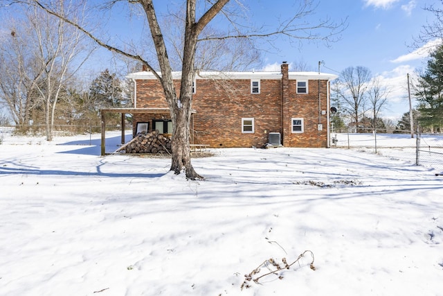 snow covered house with brick siding, a chimney, and cooling unit