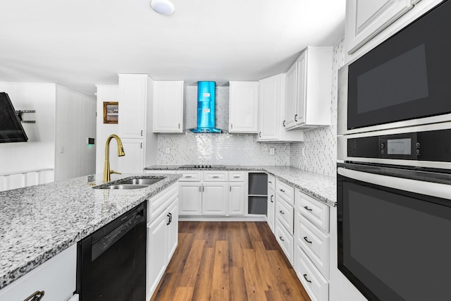 kitchen with wall chimney exhaust hood, light stone countertops, black appliances, white cabinetry, and a sink