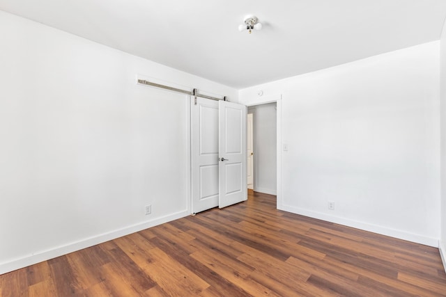 unfurnished room featuring dark wood-style floors, baseboards, and a barn door