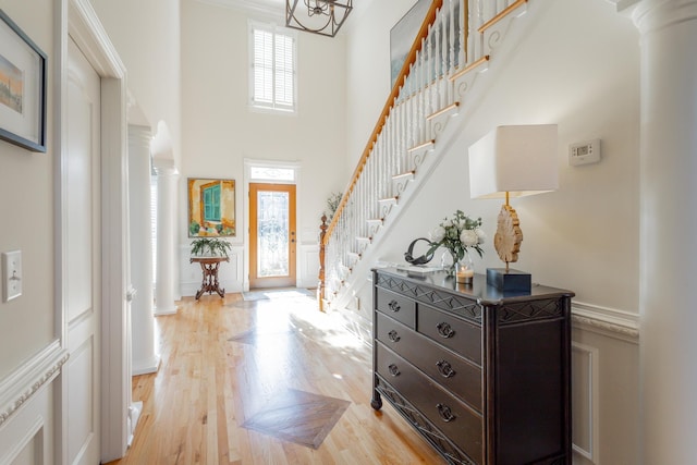 entrance foyer featuring ornate columns, light wood-style flooring, stairs, and a high ceiling