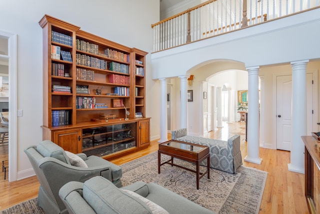 living room featuring arched walkways, light wood-style flooring, decorative columns, and baseboards