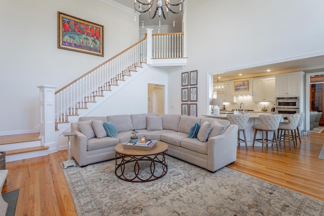 living area featuring ornamental molding, light wood-style flooring, an inviting chandelier, and stairs