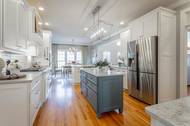 kitchen with white cabinets, a kitchen island, appliances with stainless steel finishes, decorative light fixtures, and a peninsula