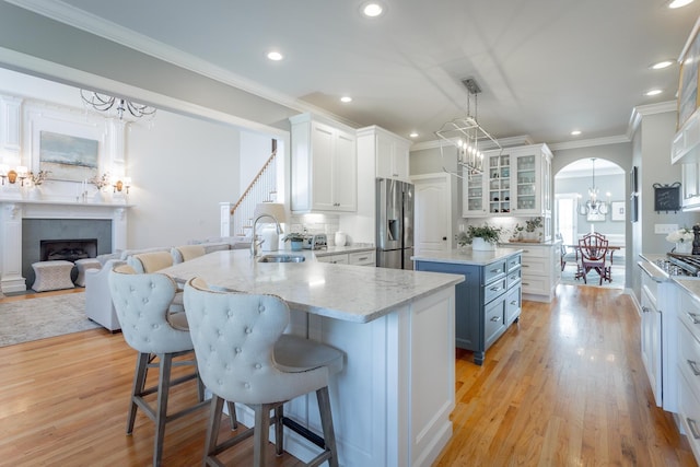 kitchen with stainless steel appliances, a sink, white cabinetry, a kitchen bar, and glass insert cabinets