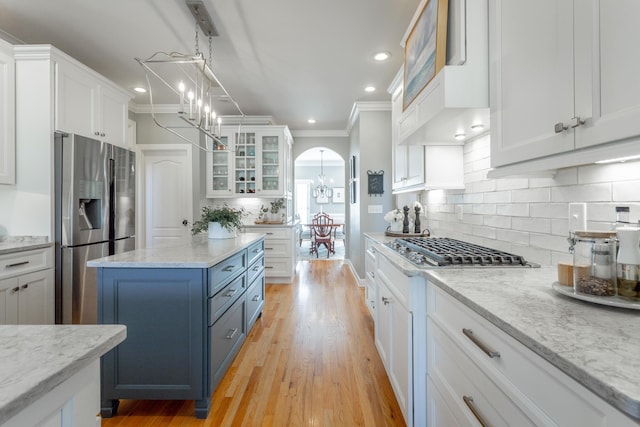 kitchen featuring white cabinets, stainless steel appliances, glass insert cabinets, and an inviting chandelier