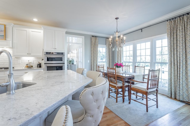 kitchen featuring white cabinets, decorative light fixtures, light stone countertops, crown molding, and a sink