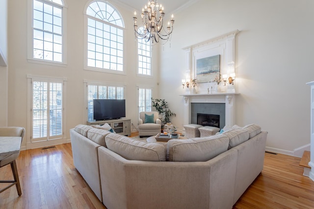 living room with a chandelier, a fireplace, a towering ceiling, baseboards, and light wood-type flooring