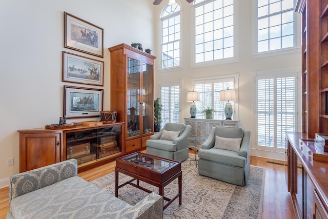 living room featuring a towering ceiling, light wood-style floors, ceiling fan, and baseboards