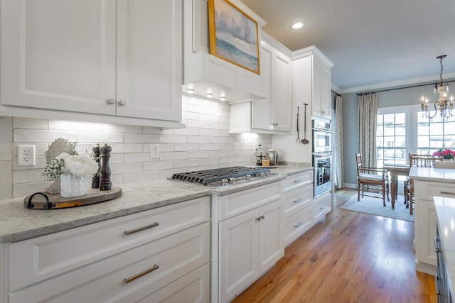 kitchen with light stone counters, stainless steel appliances, decorative backsplash, white cabinetry, and a chandelier