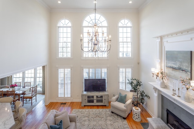 living area featuring a fireplace with flush hearth, a notable chandelier, light wood-style floors, and crown molding