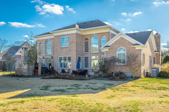 view of front of house featuring central AC, brick siding, a chimney, and a front yard