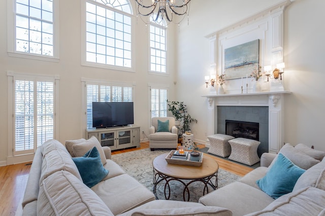 living area with a tile fireplace, light wood-style flooring, baseboards, and an inviting chandelier