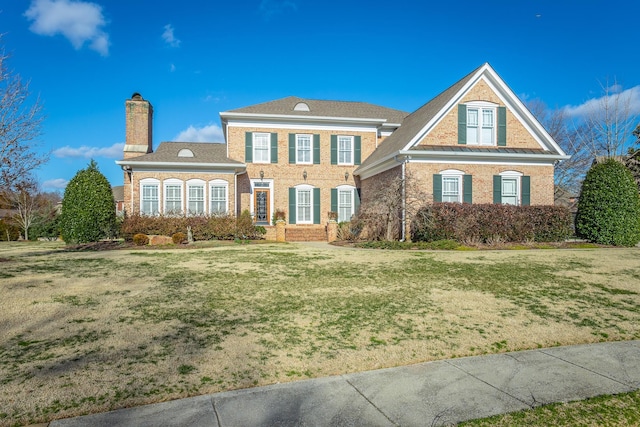 view of front of property featuring brick siding, a chimney, and a front yard