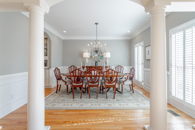 dining room featuring a wainscoted wall, light wood finished floors, and ornate columns