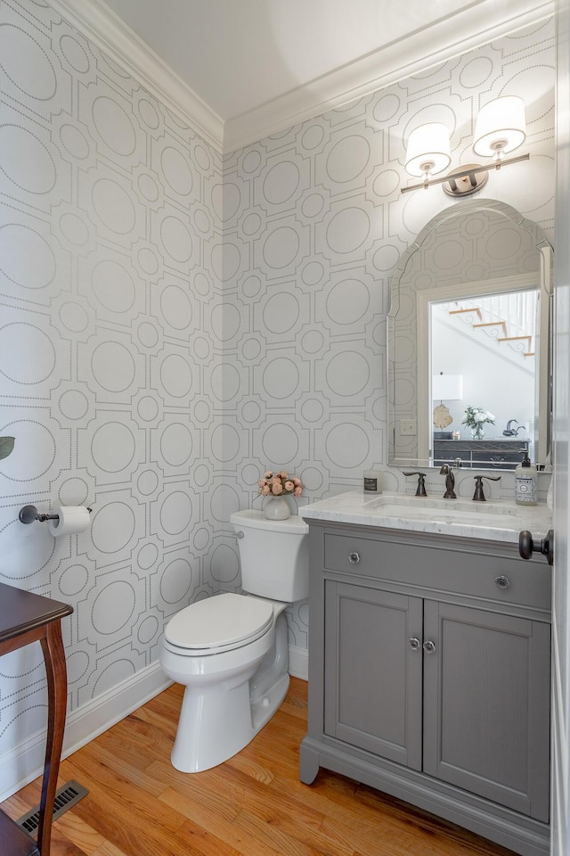 half bathroom featuring toilet, wood finished floors, vanity, visible vents, and crown molding