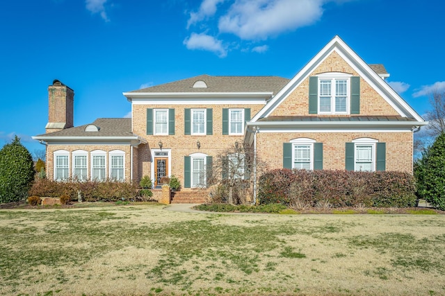 view of front of house featuring brick siding, a chimney, and a front yard