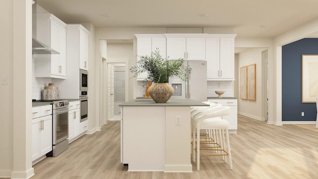 kitchen with stainless steel appliances, white cabinetry, light wood-type flooring, an island with sink, and a kitchen bar