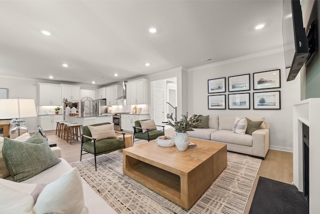 living area featuring a fireplace, light wood finished floors, recessed lighting, ornamental molding, and baseboards